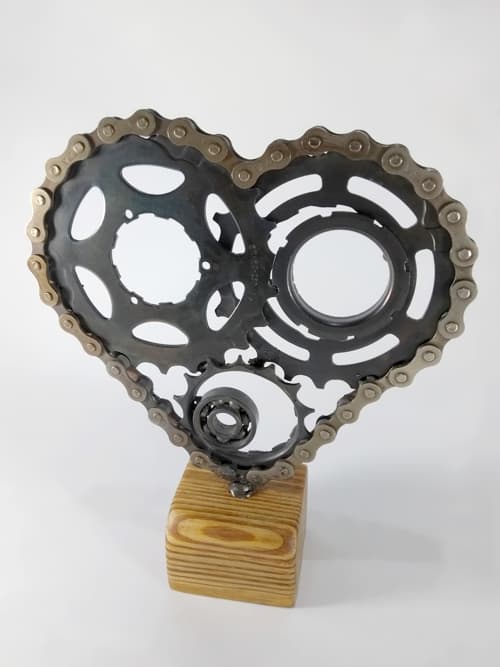 Realizado con base de pinotea de 5x5x4cm (alto) y repuestos de bicicletas que fueron reciclados. Tiene un tratamiento de pavonado lo que impide que la obra se oxide con el transcurso del tiempo. La base está cortada, lijada y encerada de forma manual y artesanal.